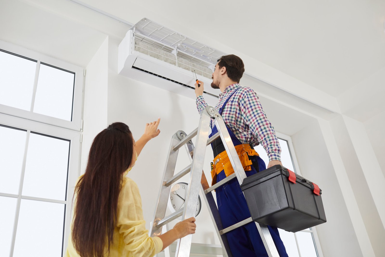 Technician from the repair service fixes the air conditioner in a young woman's home